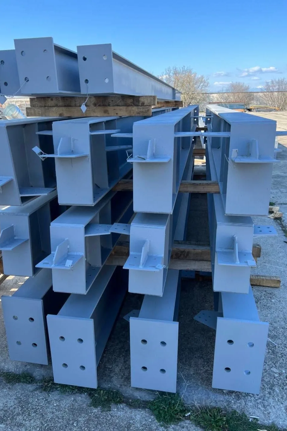 Painted structural beams and columns with bolted end plates, stacked before delivery